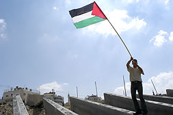 Picture for al-Ram Village - Palestine: : A young Palestinian man waves a Palestinian flag atop the blocks waiting to be erected along the roadway from Jerusalem to Ramallah.
